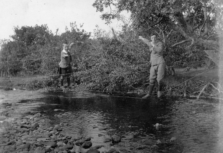 Young man + boy crossing a burn on suspended wire